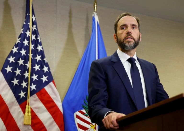 Special Counsel Jack Smith speaking at a podium with the U.S. flag and Justice Department flag behind him during a press briefing.