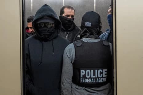 Federal agents wearing tactical gear and masks stand inside an elevator during an immigration enforcement operation.
