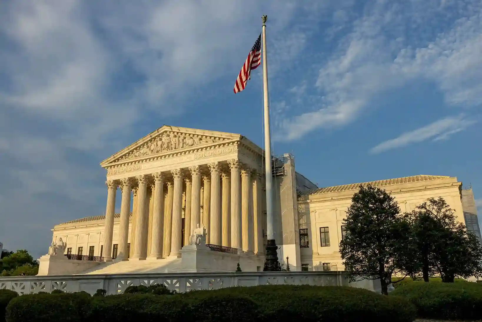 The U.S. Supreme Court building with the American flag waving above the front steps on a clear day.