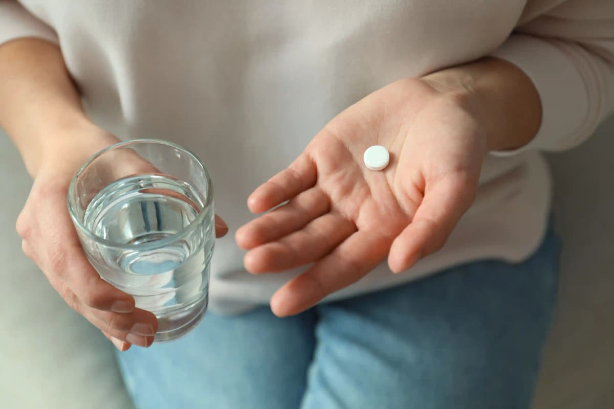 Person holding an abortion medication pill in one hand and a glass of water in the other