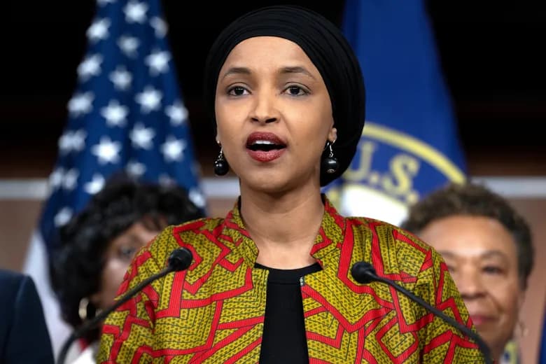Congresswoman Ilhan Omar speaking at a press conference with American flags in the background
