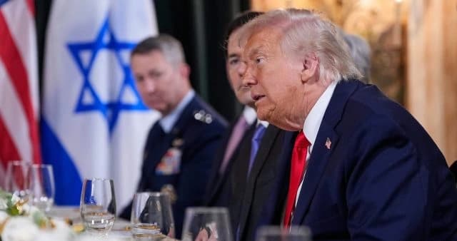 U.S. President Donald Trump engaged in a discussion with Israeli officials at a dinner, with the Israeli flag visible in the background.
