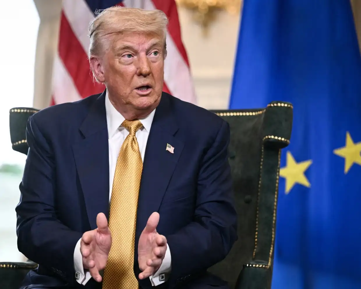 Donald Trump speaking during an interview with U.S. and European Union flags in the background