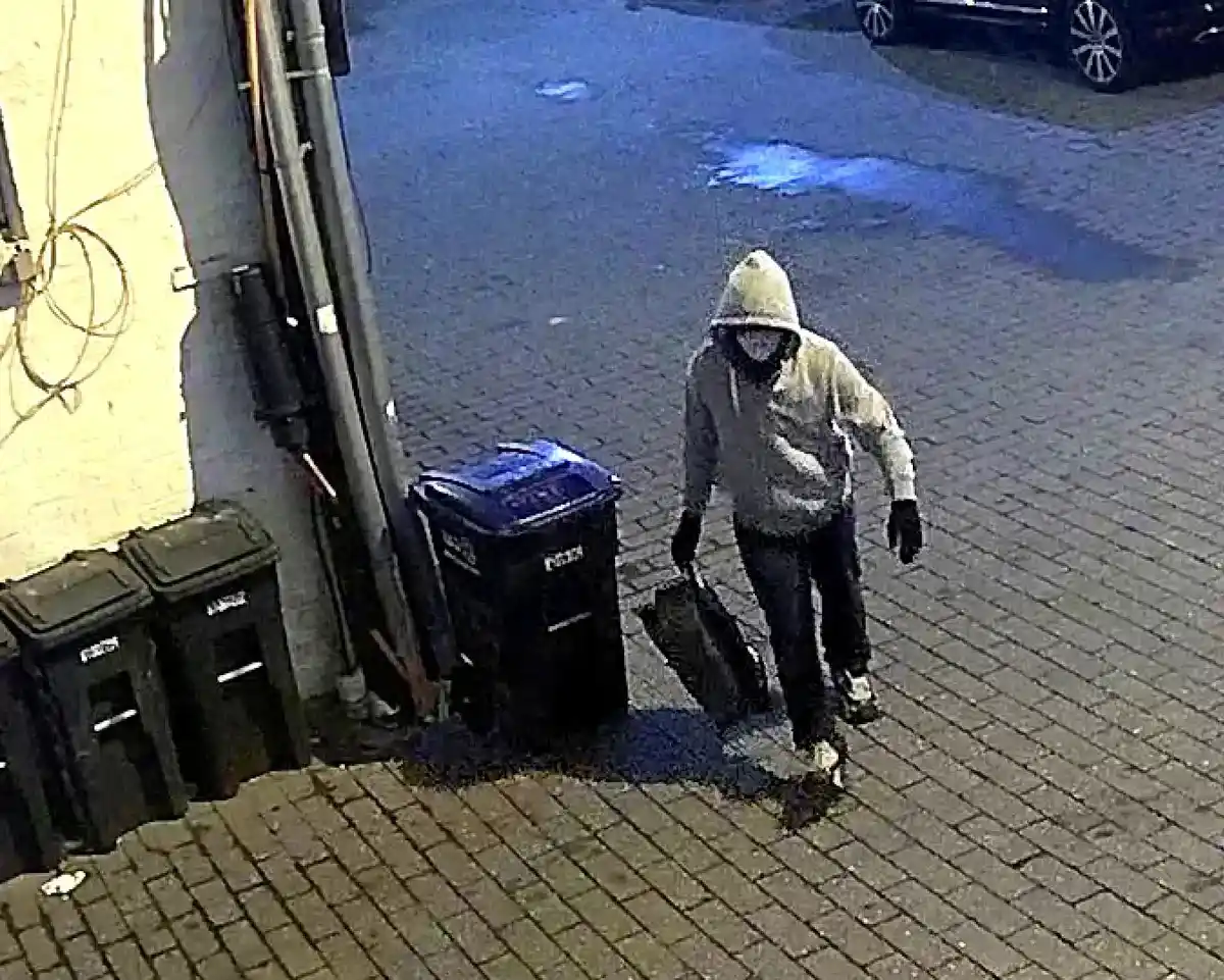 Surveillance footage showing a hooded individual carrying a bag near trash bins in an alley during the pipe bomb investigation.