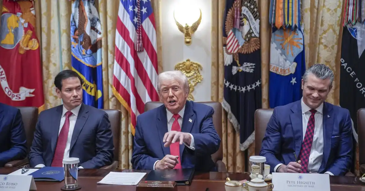 President Donald Trump speaking during a meeting with U.S. officials as flags and military insignias are displayed in the background.